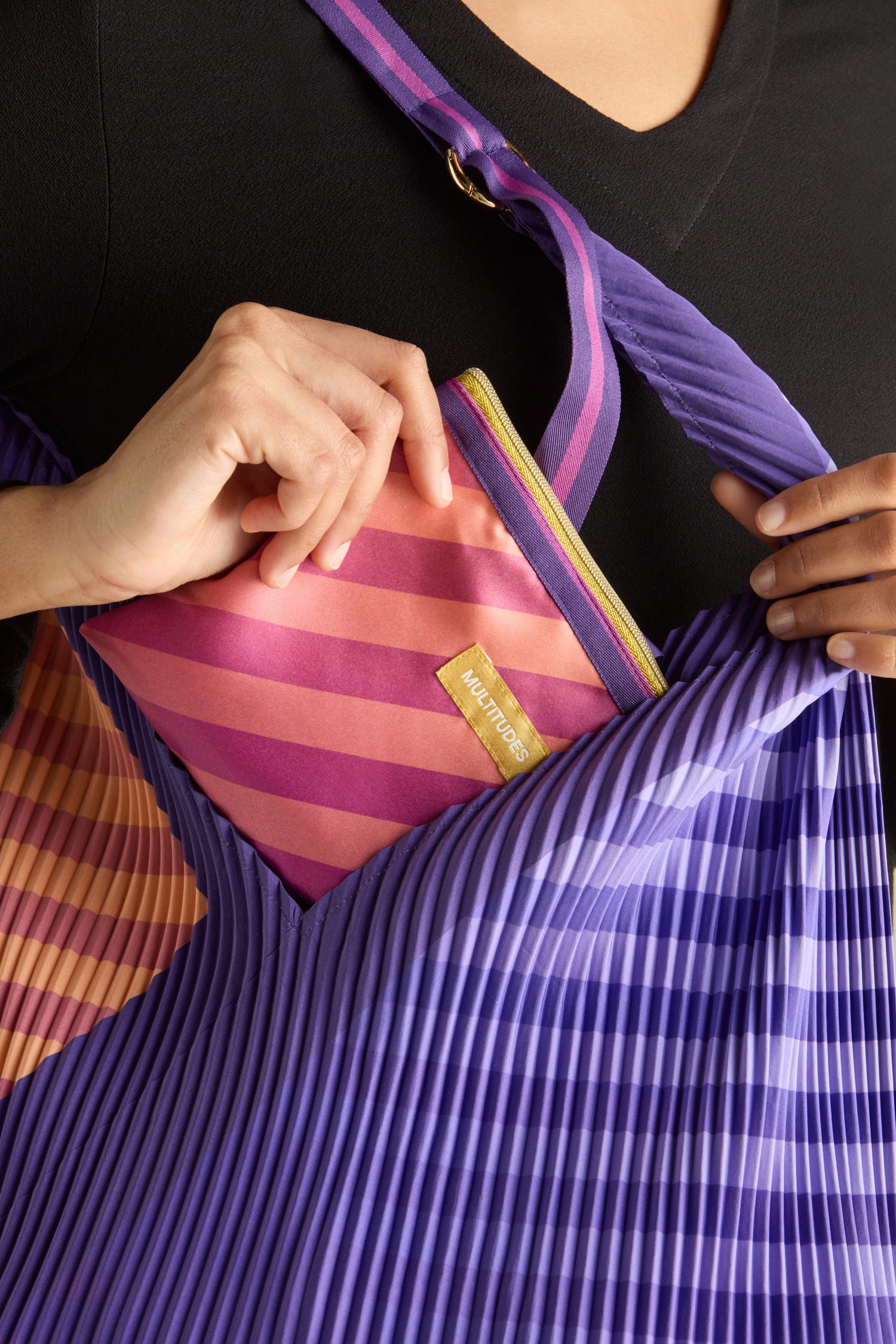 Someone places a pink striped pouch into the Pleated Y Handbag, opting for eco-friendly fashion with this chic recycled accessory.