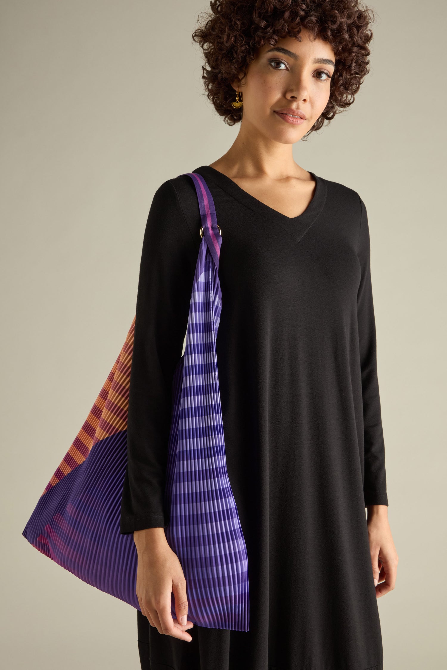 A person in a black dress holds the Pleated Y Handbag, a large, colorful striped bag that combines stylish design with eco-friendly materials.