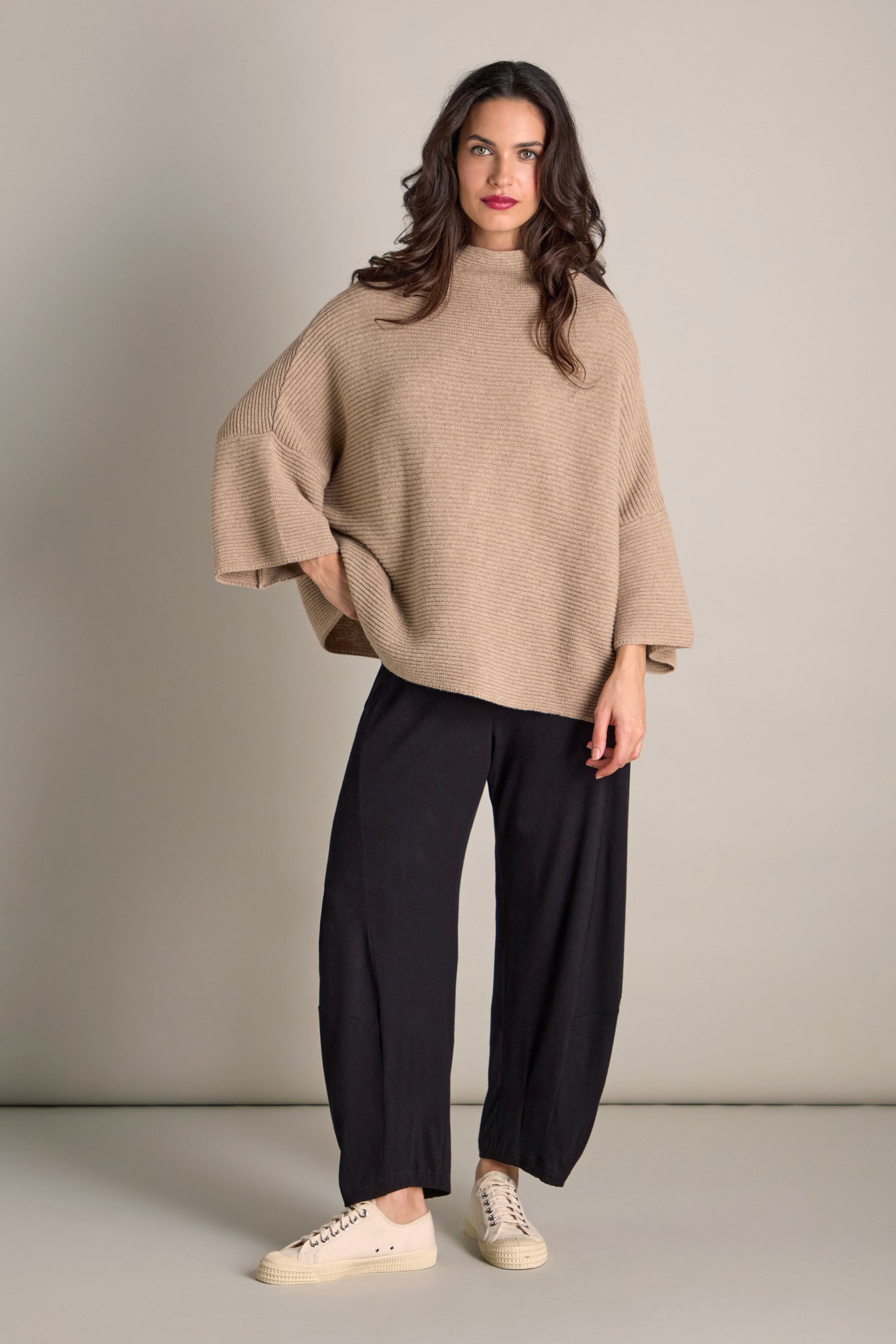 A person stands against a plain background, exuding cozy comfort in the Pauline Rib Boxy Knit, paired with black wide-leg pants and beige sneakers.