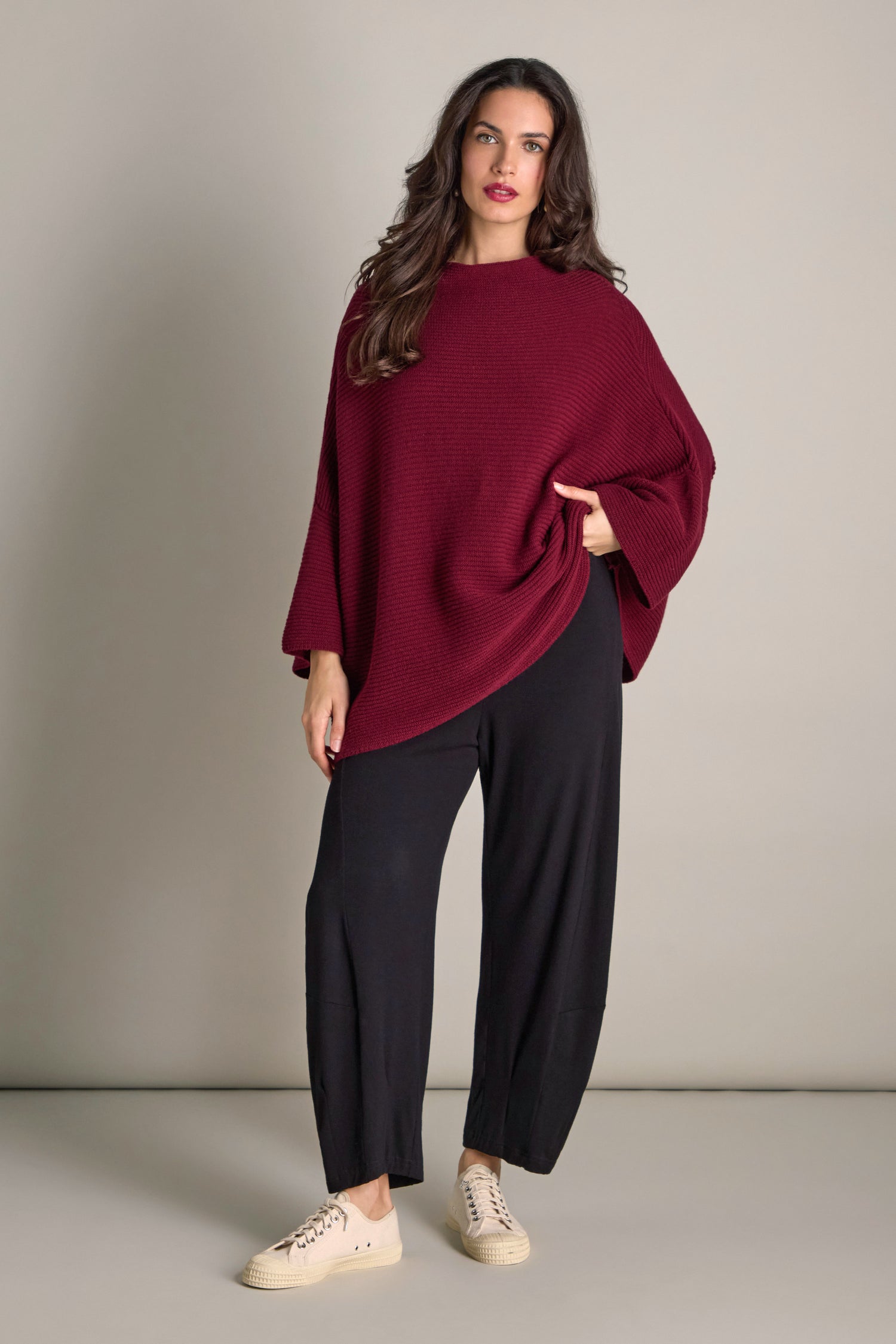 A woman in a red Pauline Rib Boxy Knit sweater and black pants stands against a neutral background.