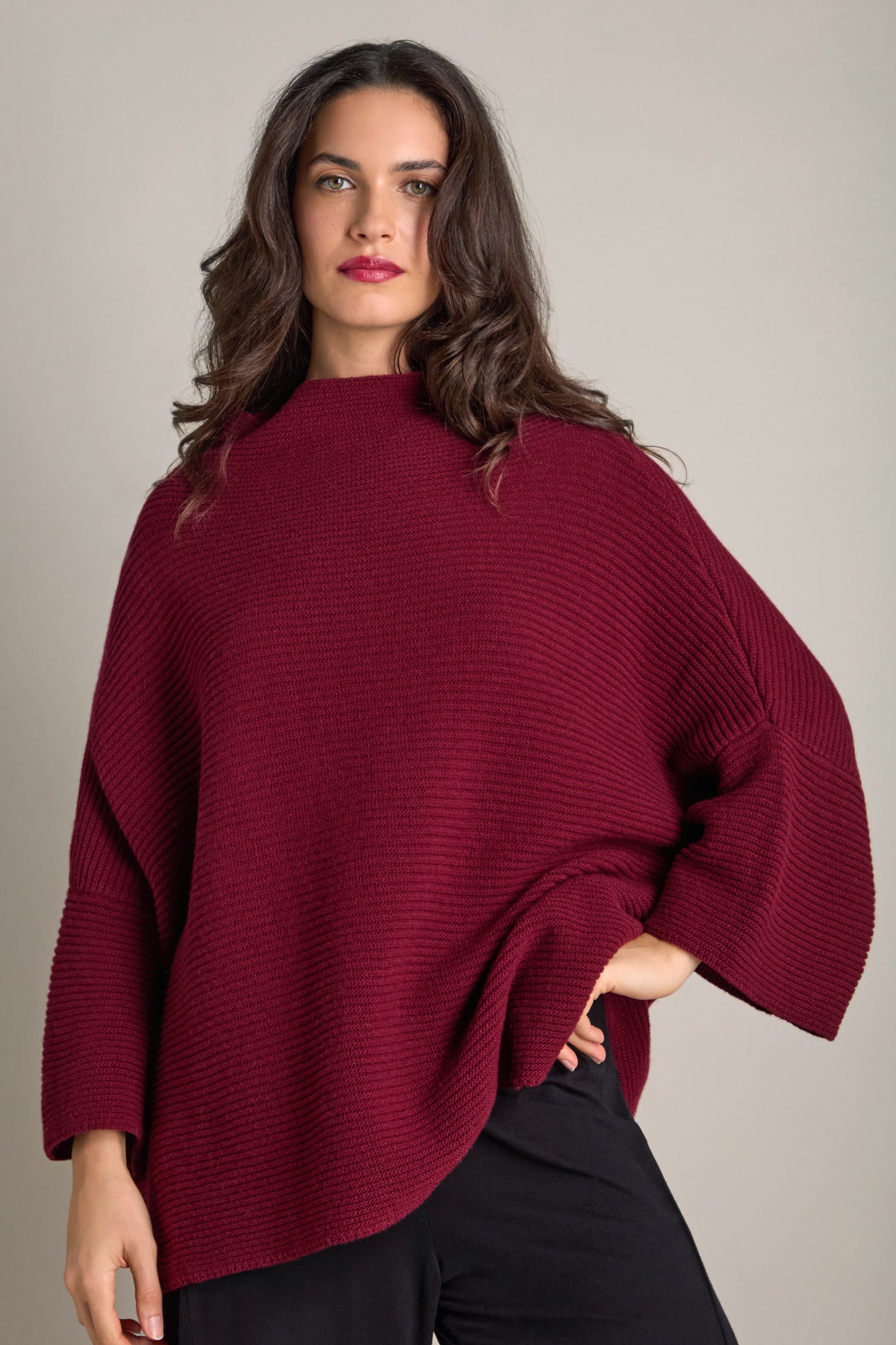 A person wearing the Pauline Rib Boxy Knit sweater in a rich burgundy hue stands against a neutral background, exuding cozy comfort.