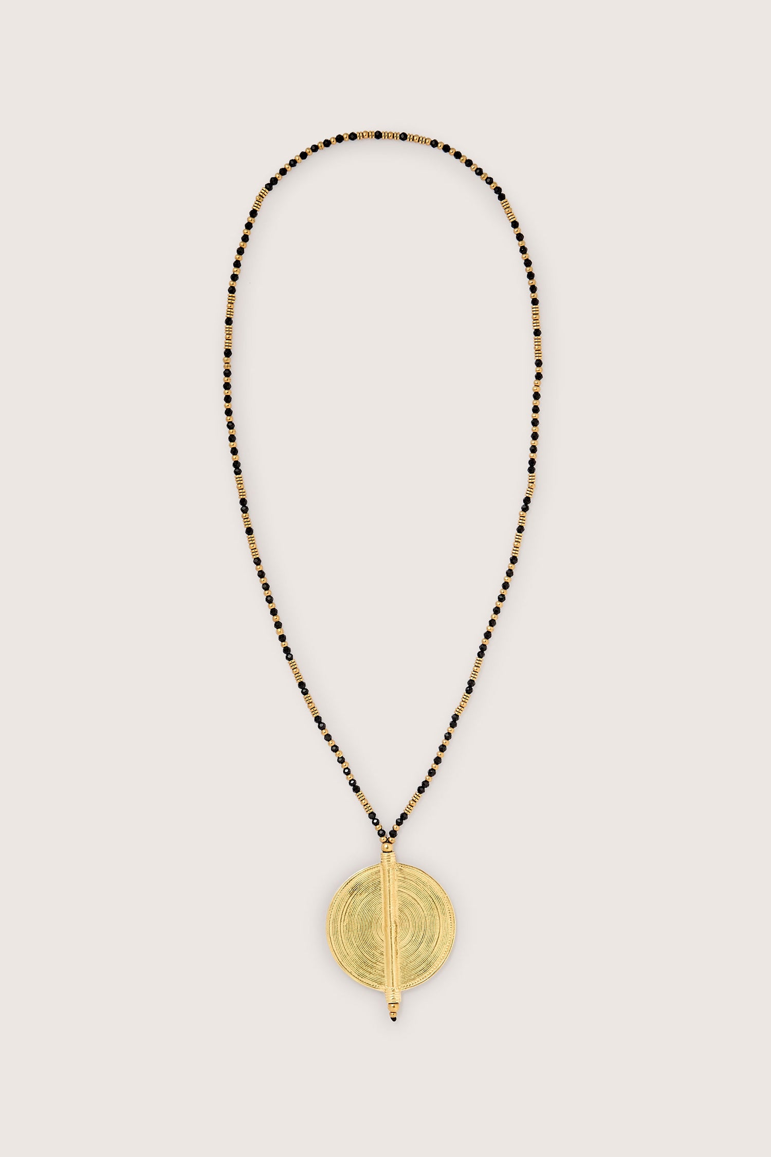 The Spiral Pendant, meticulously handcrafted by skilled artisans, showcases a gold pendant on a long, slender beaded necklace adorned with an elegant design of gold and black beads.