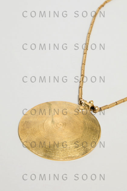 The Long Spiral Pendant (model NCCCE170) features concentric engraved lines on a gold circular pendant with a gold chain, displayed on a light background with repeated "COMING SOON" text overlay.