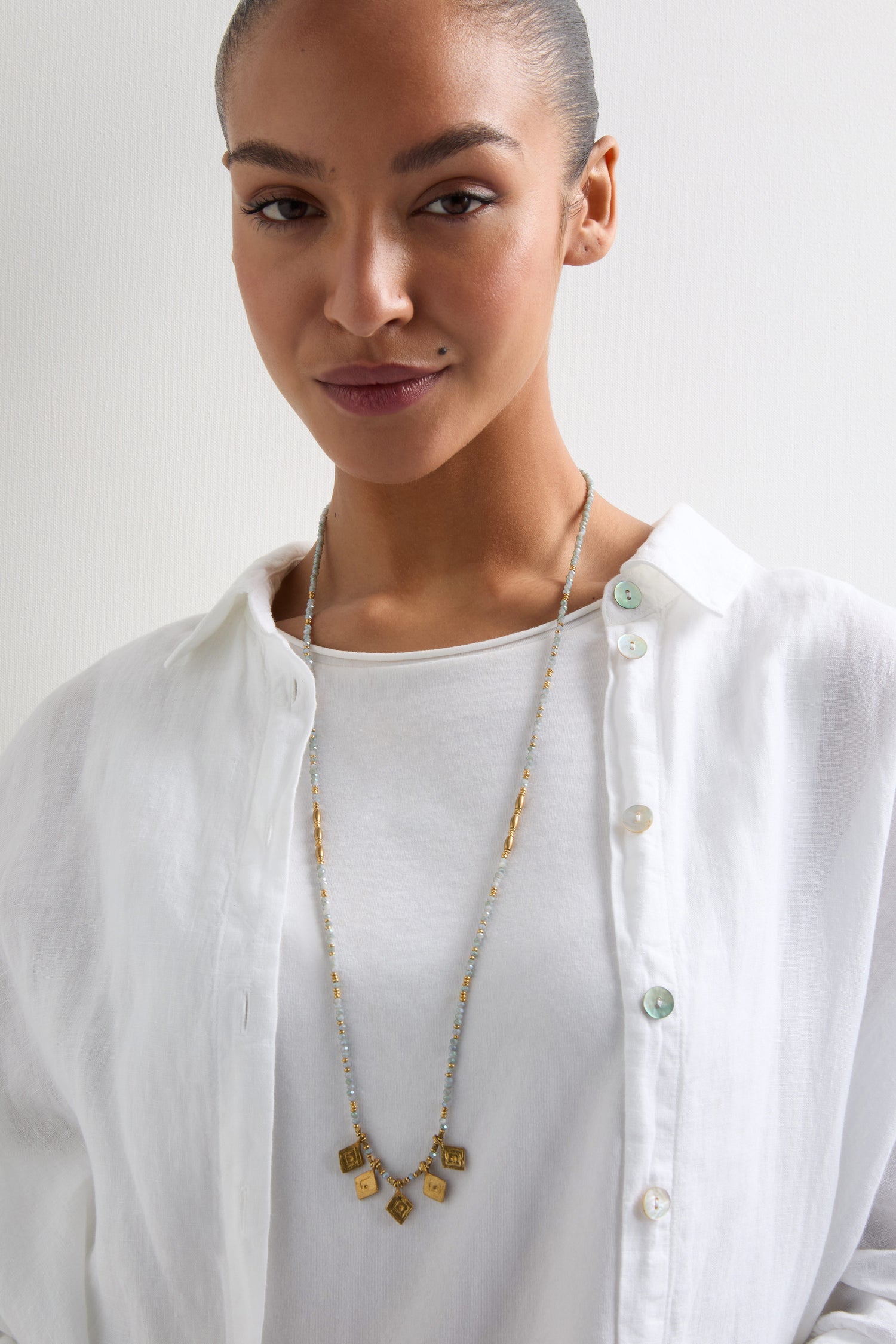 A woman wearing a white shirt and the Eanna Bead Pendant necklace stands against a plain background.