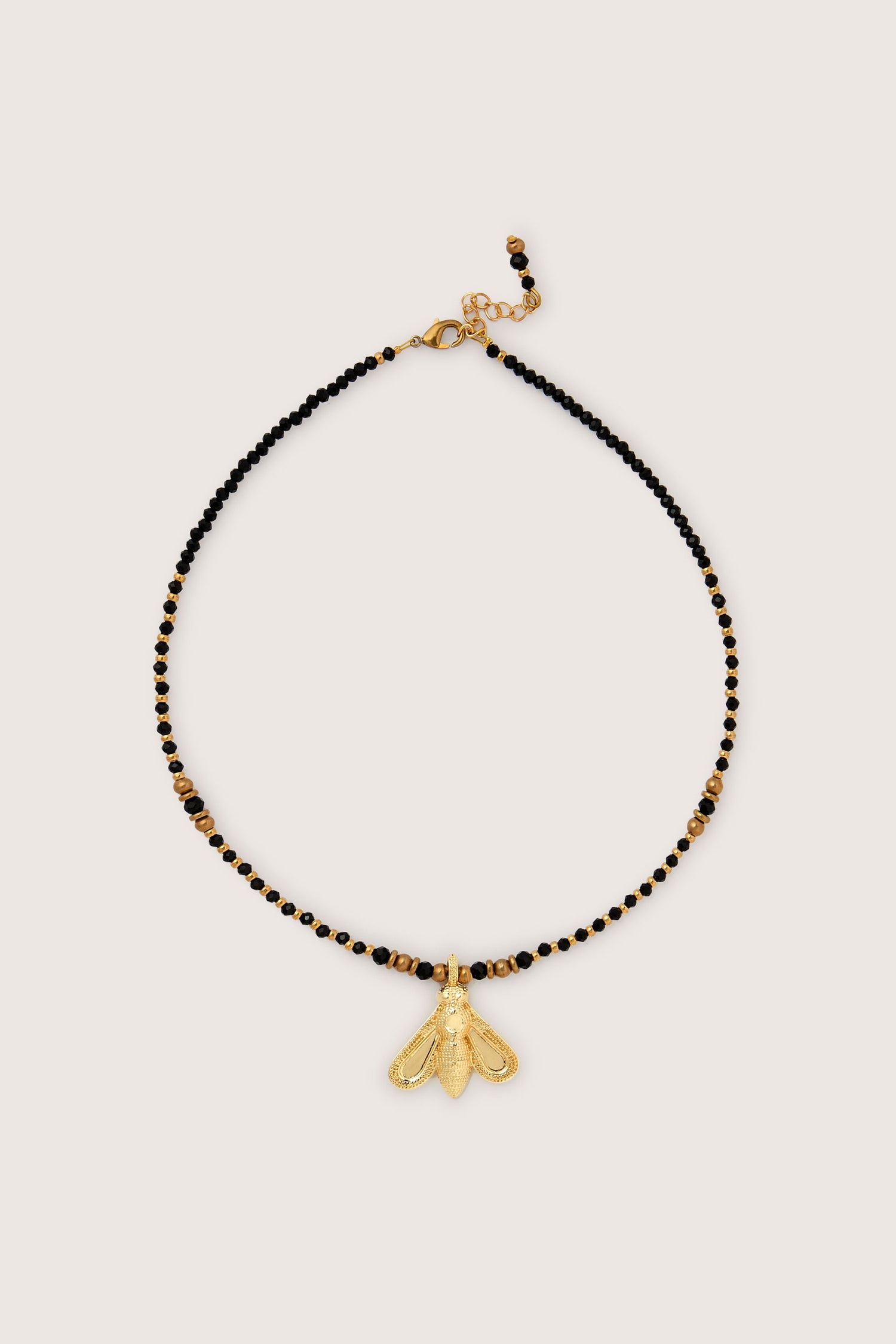 The Bumblebee Necklace is adorned with gold beads and black accents, showcased by a prominent gold bumblebee pendant, set against a light beige background.