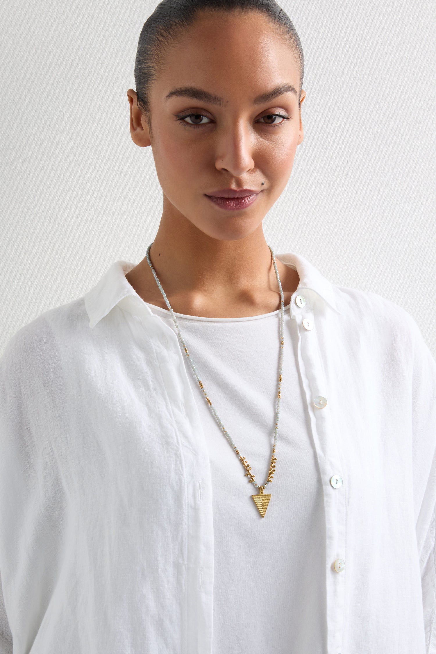 A person wearing a white shirt stands against a plain background, showcasing the Triskel Bead Pendant with its pearlescent grey beads.