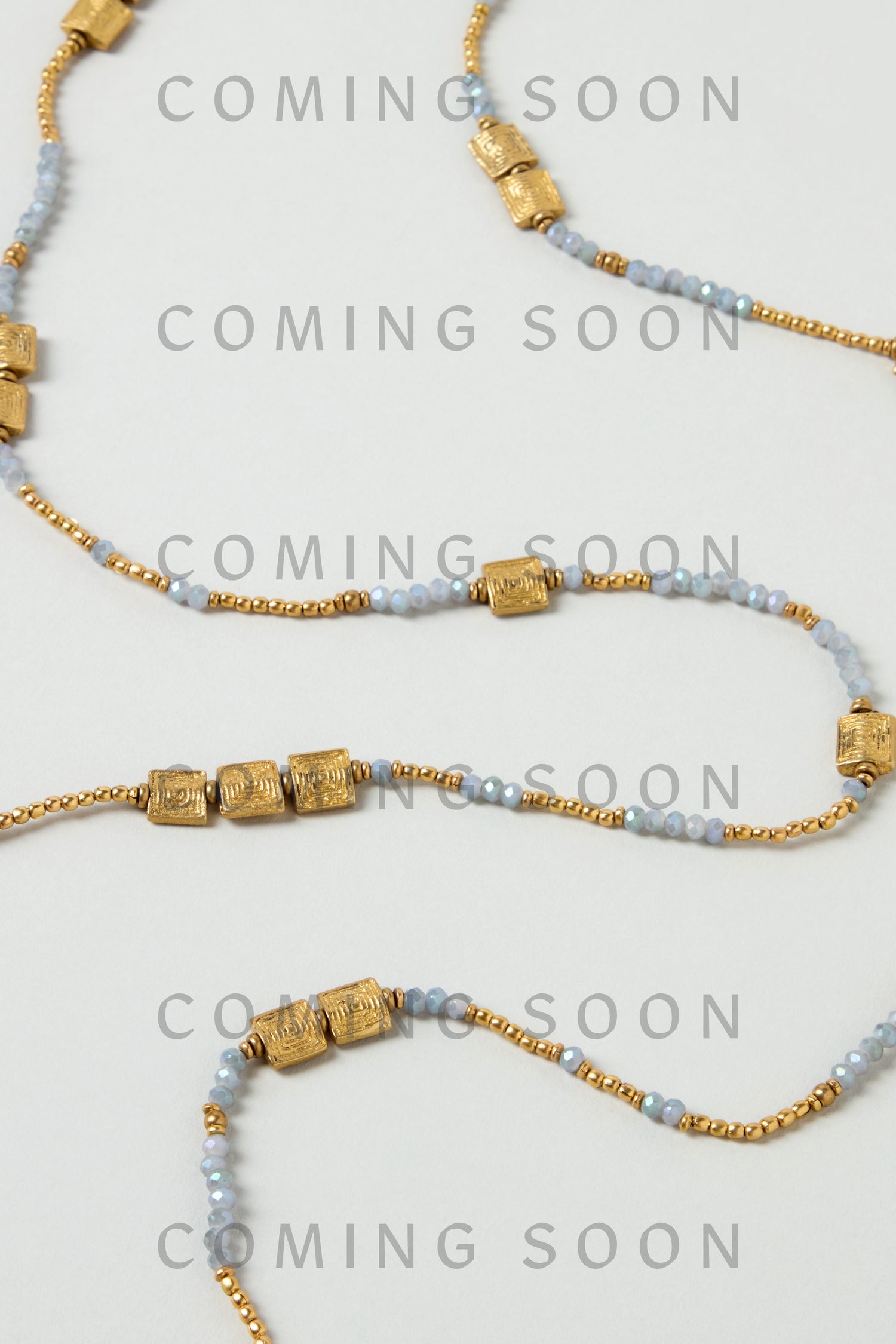 The Engraved Squares Bead Necklace, featuring gold cylindrical and small blue beads, is displayed on a white background with the code NCCCE544 and "COMING SOON" overlaid.