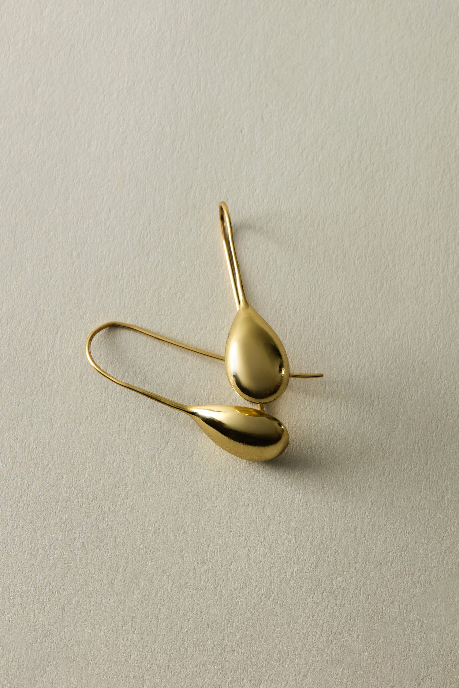 Ideal for a chic summer look, the Gold Gilded Teardrop Earrings rest gracefully on a light textured surface.