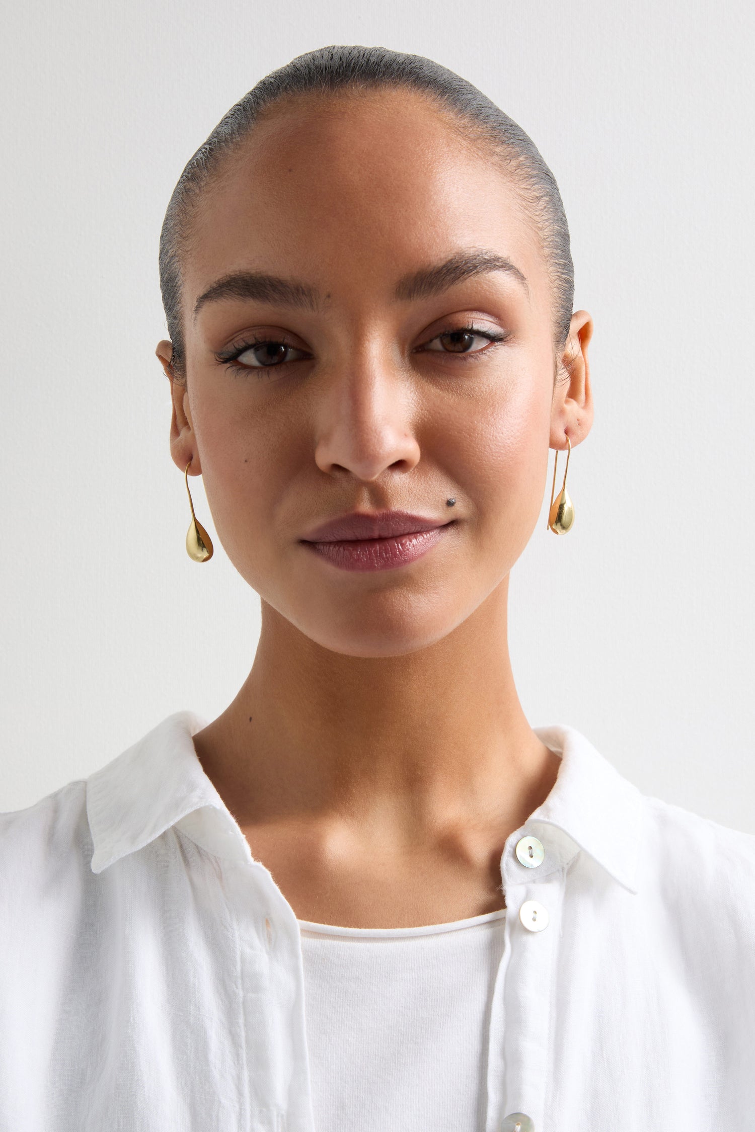 Someone with tied-back hair is wearing a white collared shirt and elegant Gold Gilded Teardrop Earrings, facing the camera against a plain backdrop.