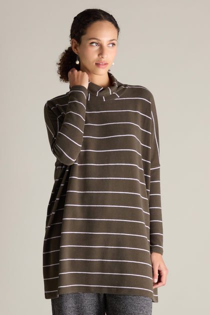 A person is wearing a Narrow Stripe Polo Tunic featuring long sleeves and olive green with white horizontal stripes, paired with gray pants, standing against a neutral background.