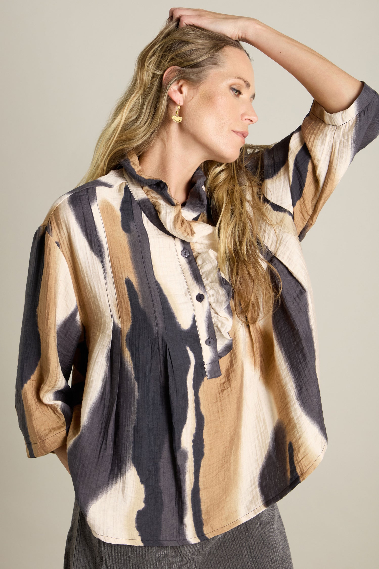 A person with long hair, wearing the Crinkle Viscose Print Blouse with a loose fit, ruffle collar, and watercolor pattern, poses while resting one hand on their head.