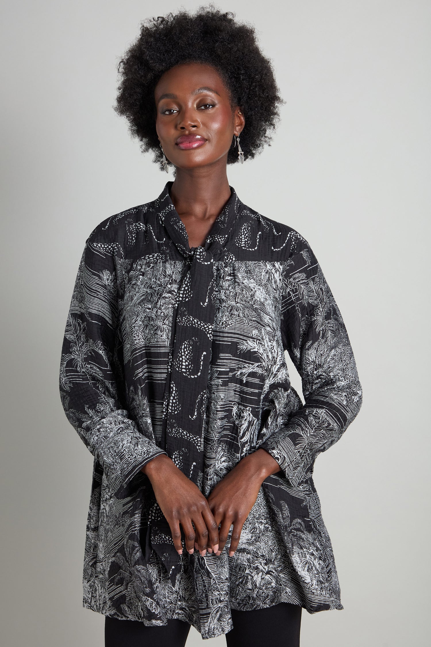 A person with curly hair stands against a neutral background, wearing Noen's Tie Neck Viscose Shirt featuring a black and white pattern.