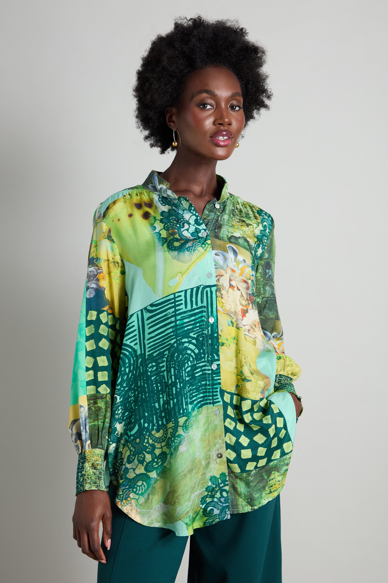 A person wearing the Patchwork Print Viscose Shirt, featuring a lively design in green, yellow, and teal tones, stands out when paired with dark green pants.