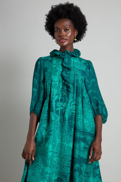 A person stands wearing the Frill Neck Viscose Dress in a green jungle-inspired print, featuring elbow-length sleeves that perfectly complement its A-line silhouette.