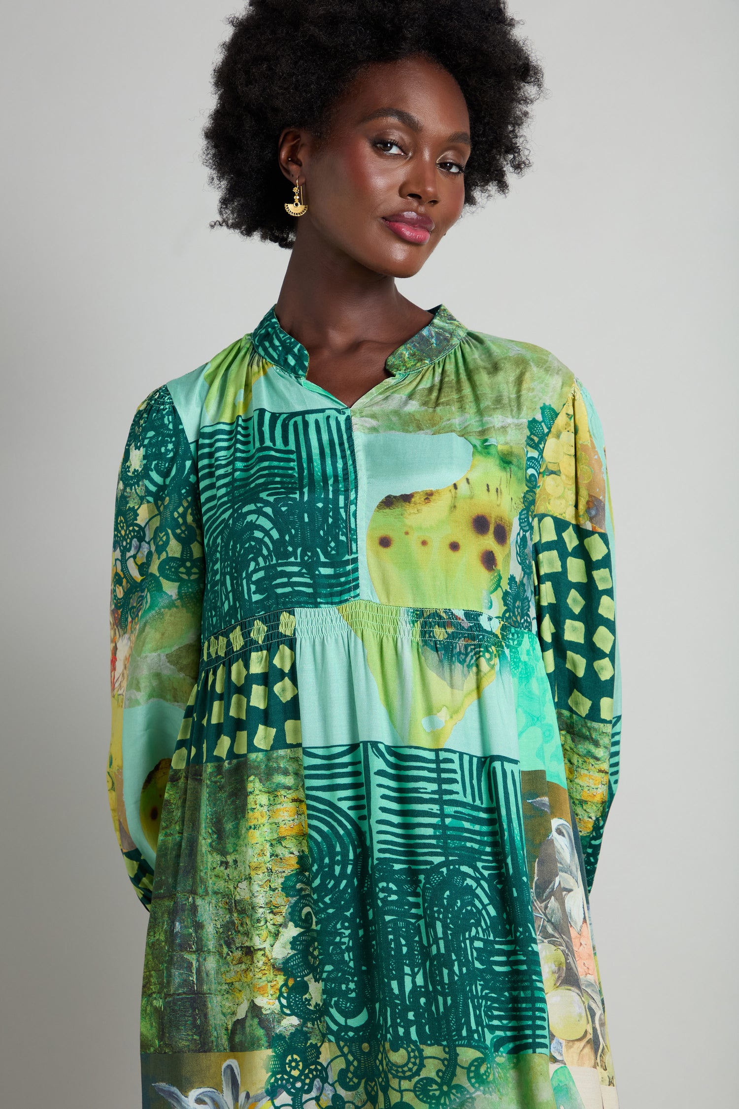 A person with an afro hairstyle wears a Patchwork Print Viscose Dress in vibrant green and yellow tones, complemented by gold earrings.