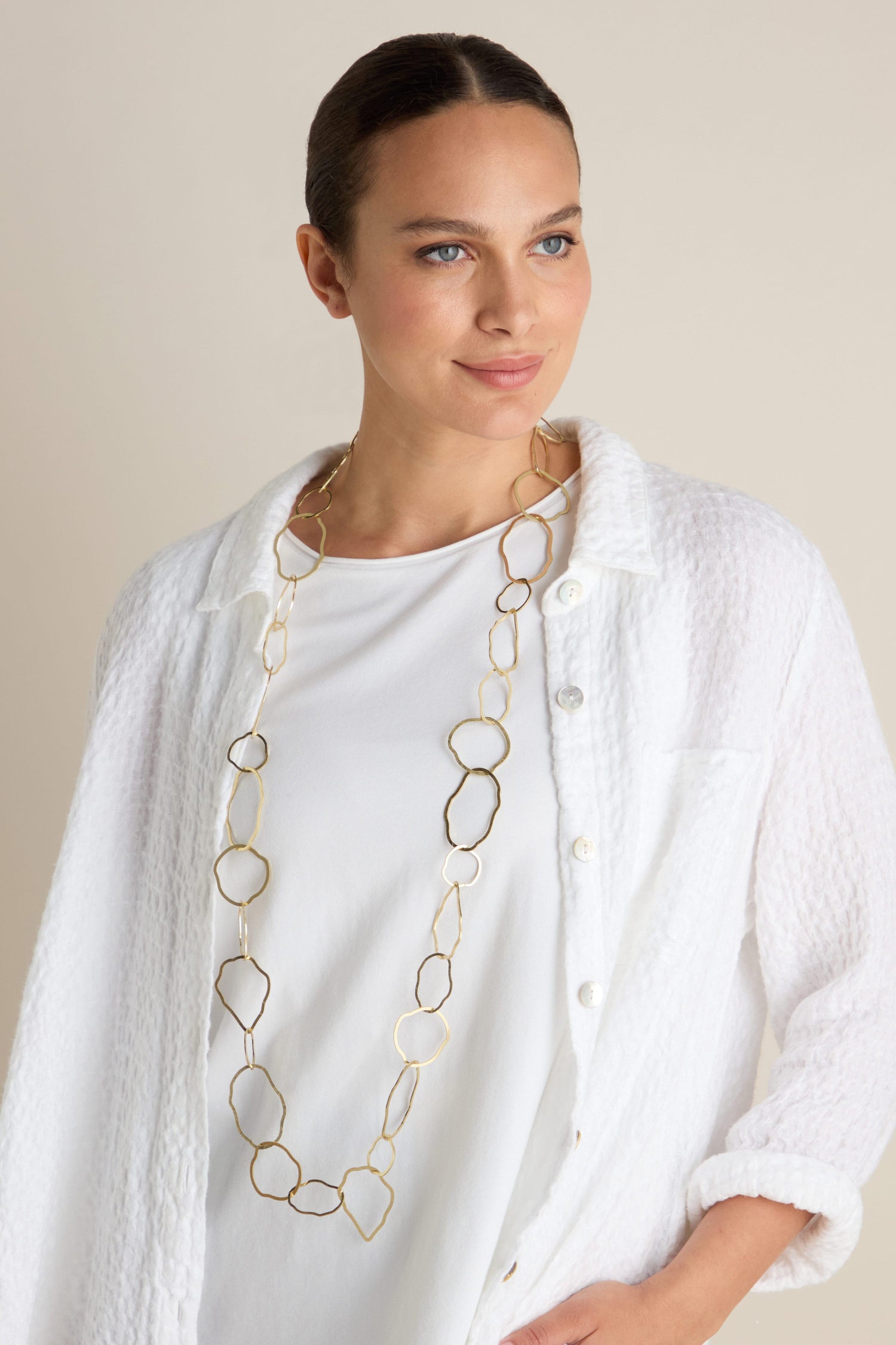 A woman wearing a white textured shirt and the Crushed Hoop Necklace rests elegantly against a neutral background.