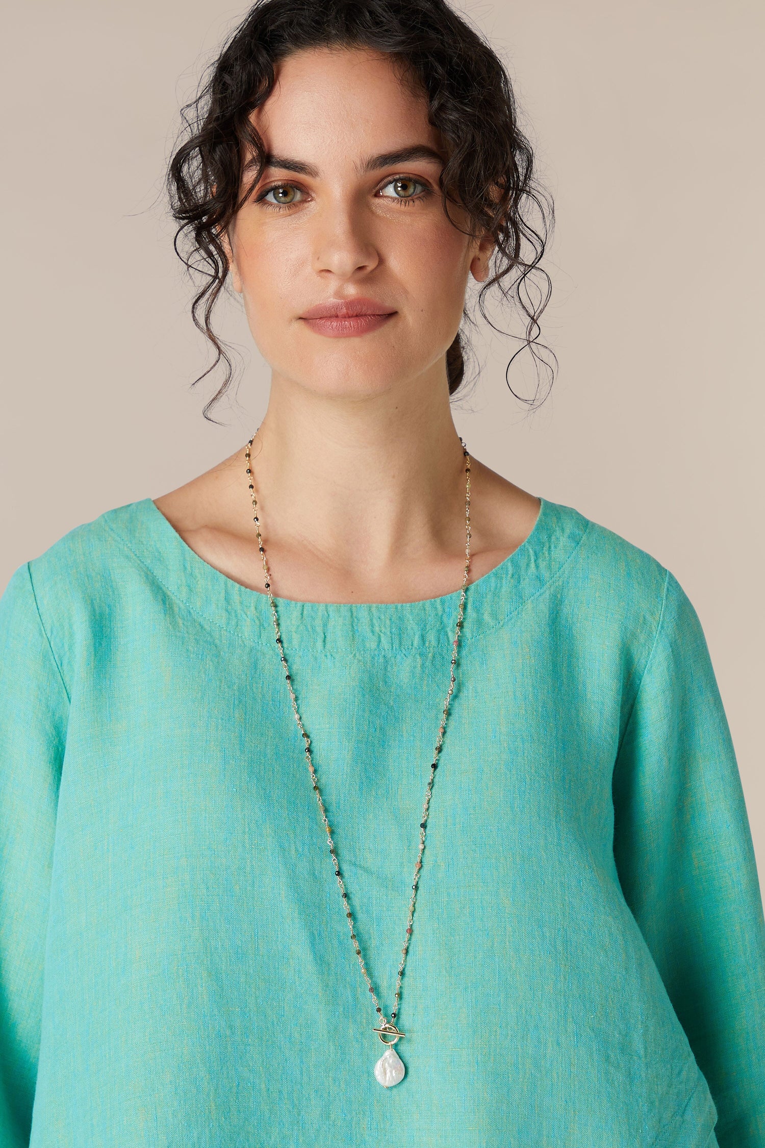 Woman in blue top with a long necklace featuring a Daisy Freshwater Pearl Pendant.