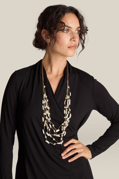 A woman with curly hair, wearing a black top and the Cascade Pearl Necklace, has one hand on her hip and is looking off to the side.