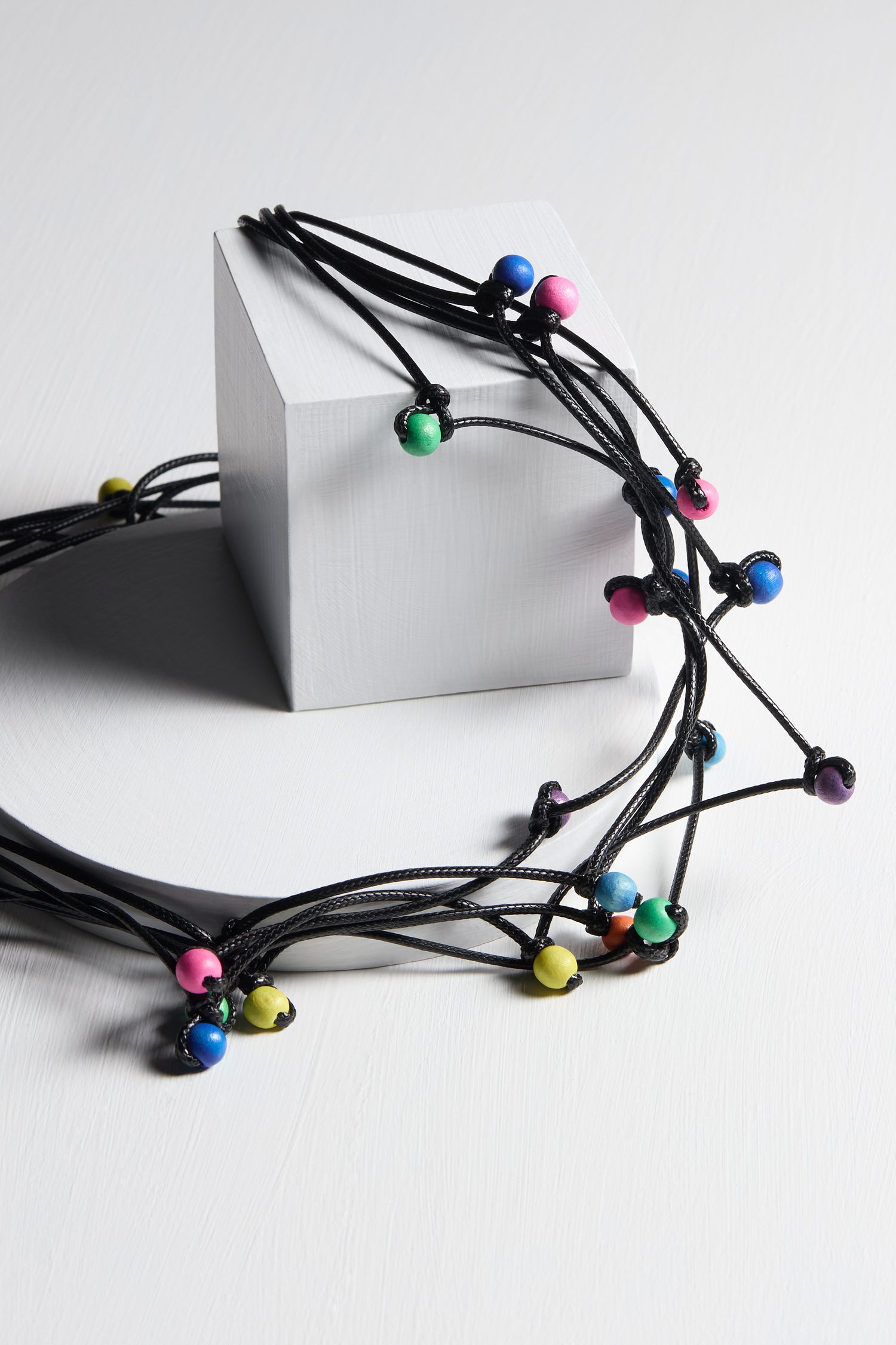 The Solar System Necklace features a white cube adorned with black cords, each thread showcasing unique accessory beads in vibrant colors such as blue, pink, green, and yellow.