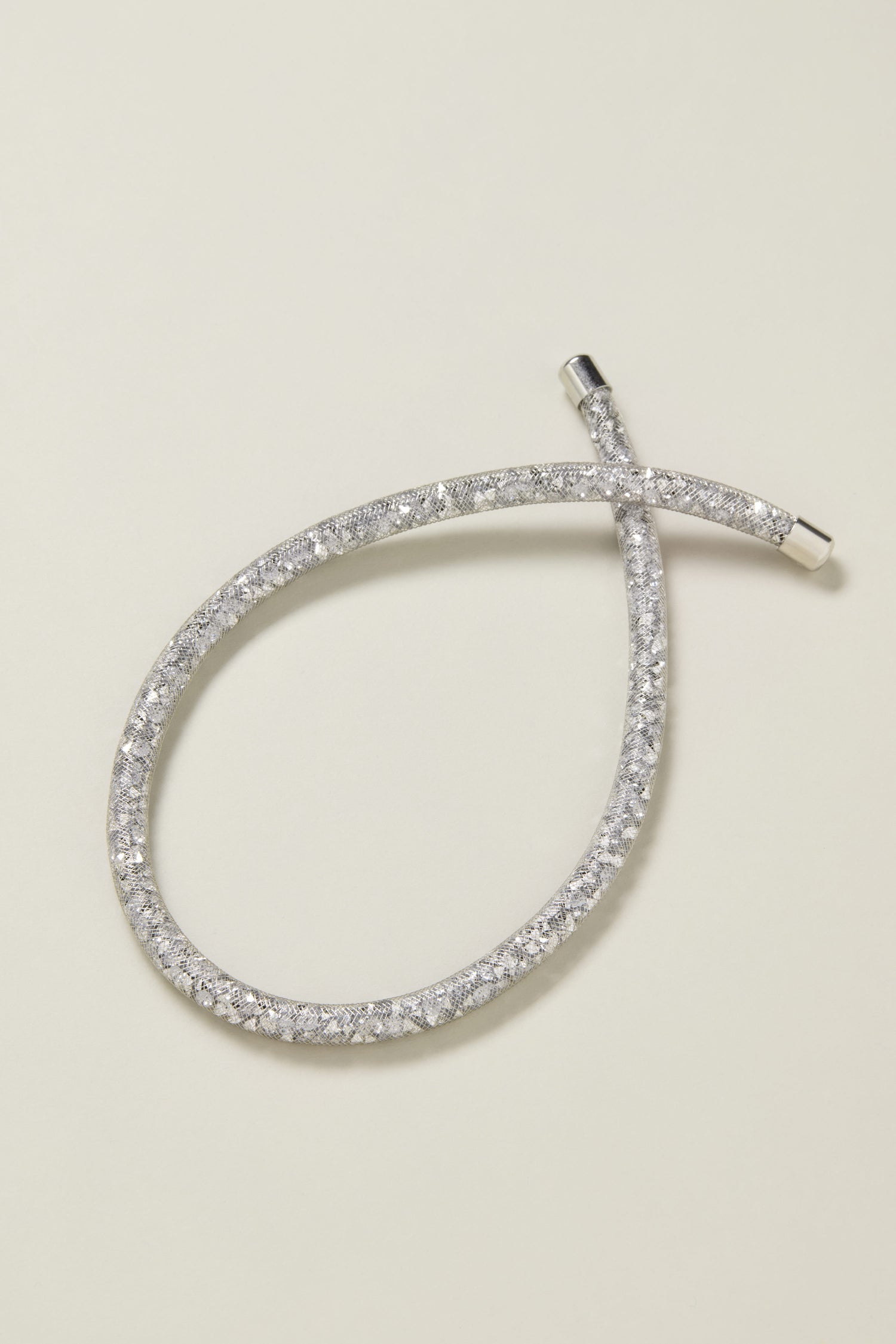 A flexible, silver-toned short diamante necklace featuring a continuous row of small, sparkling stones is displayed on a light background.