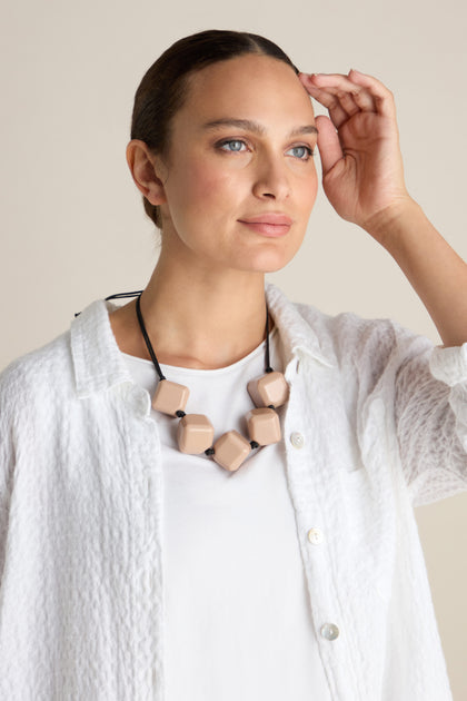 A person wearing a white shirt and the distinctive Twisted Cube Cord Necklace with large beads looks into the distance while raising their hand to their forehead.