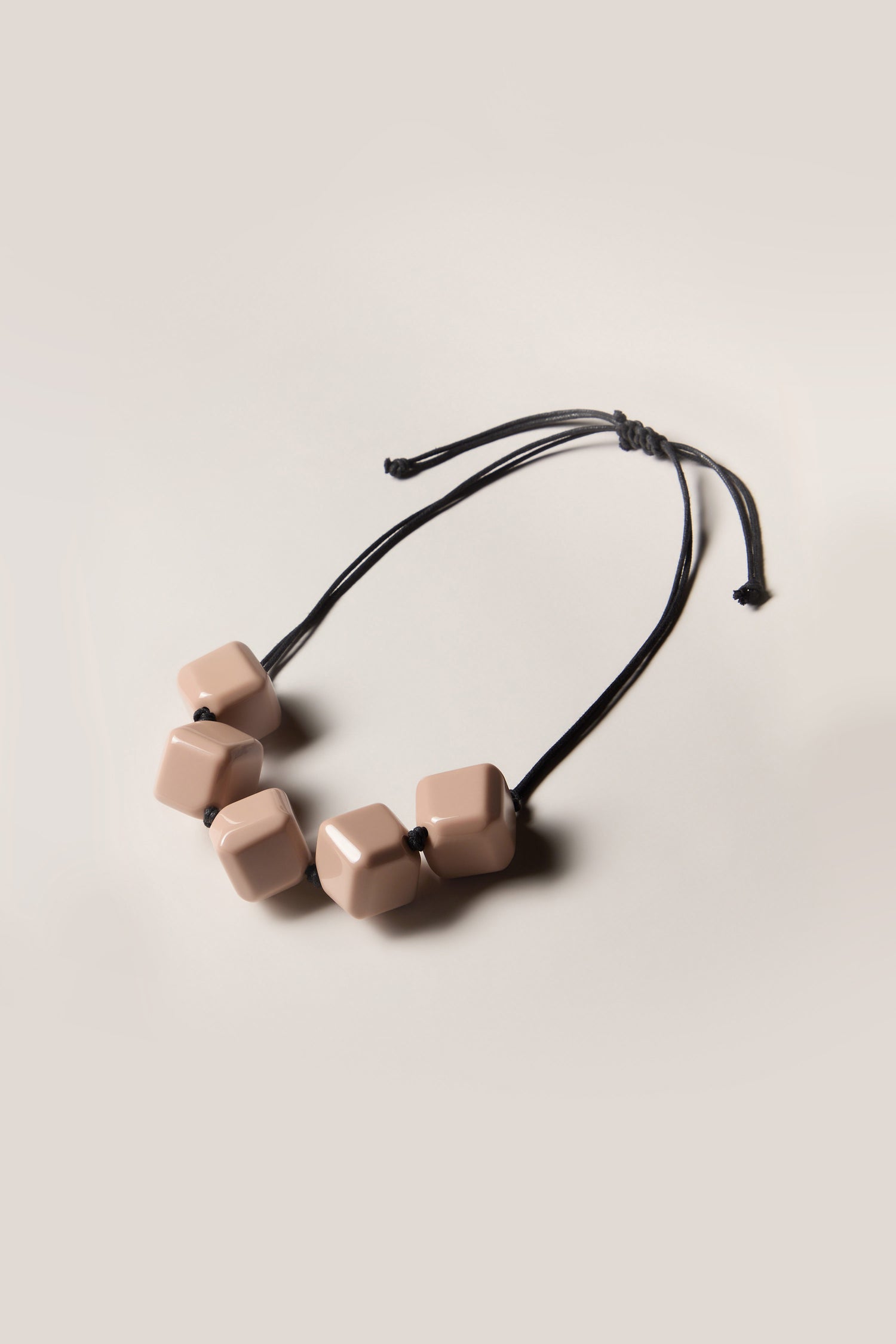 The Twisted Cube Cord Necklace is a black, adjustable piece featuring five large, light pink geometric beads that are evenly spaced along its length.