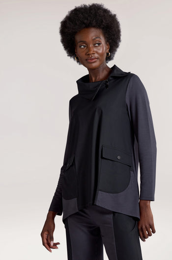 A person with short curly hair is wearing a Zip Collar Pocket Top, which features long sleeves, large pockets, zipper details, and a zip collar. They have paired it with matching black pants and are looking slightly to their left.