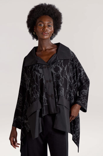 A person with an afro hairstyle is wearing the Big Pocket Wide Collar Jacket in black, featuring an abstract digital print and wide collar, paired with black pants, standing against a plain background.