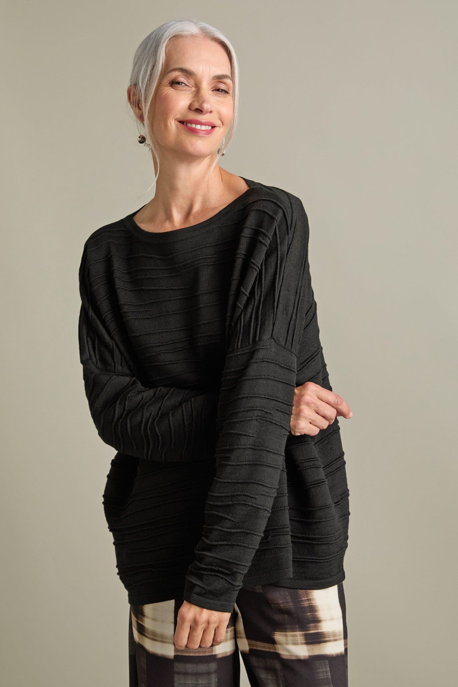 A woman with silver hair smiles while wearing the Rib Detail Wide Neck Knit and plaid pants, standing against a plain background.