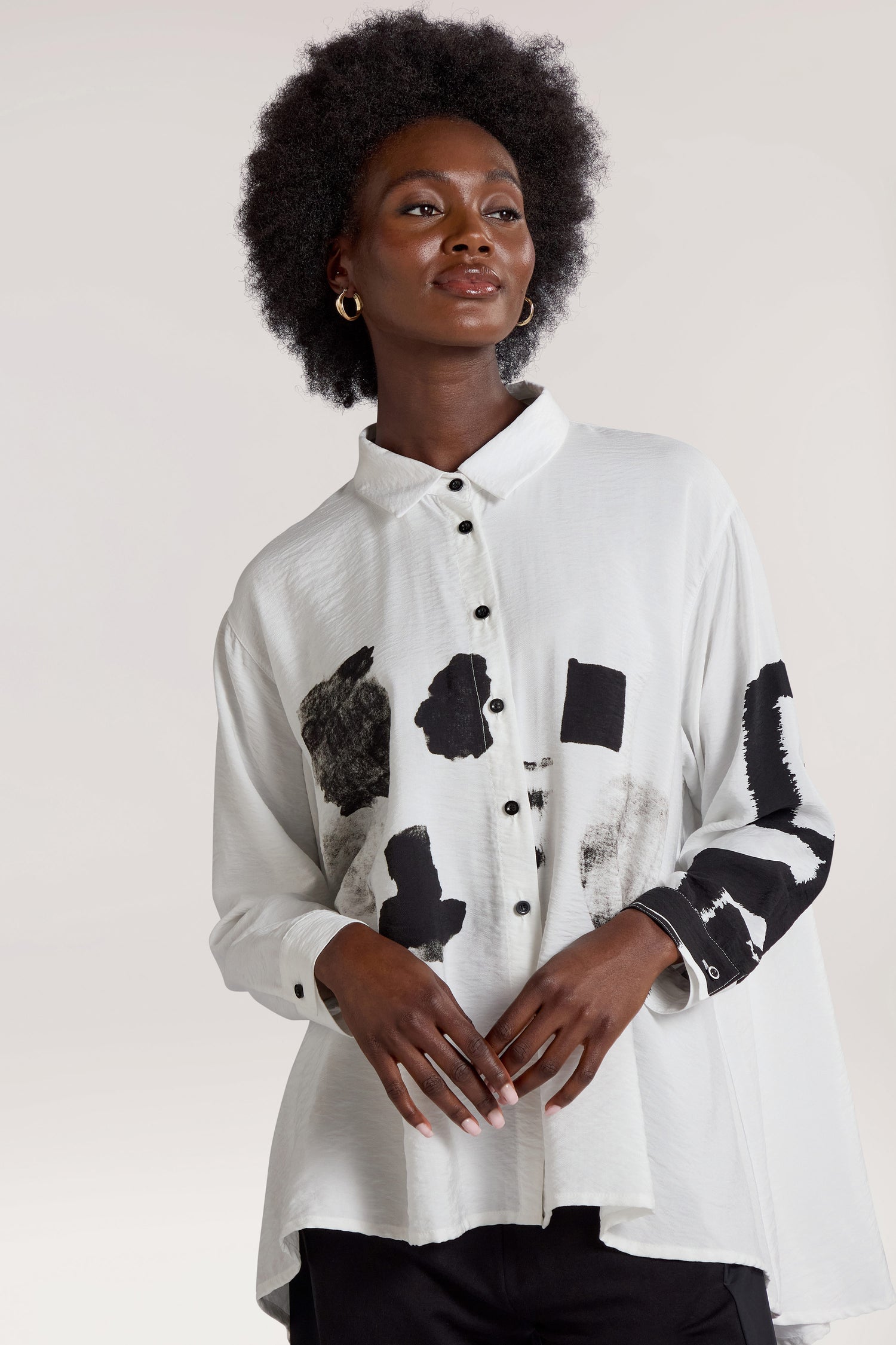 A person with a natural afro hairstyle wears the Viscose Print Easy Shirt, which boasts a contemporary design with black abstract patterns and black buttons. They stand against a neutral background, highlighting the modern aesthetic of the shirt.