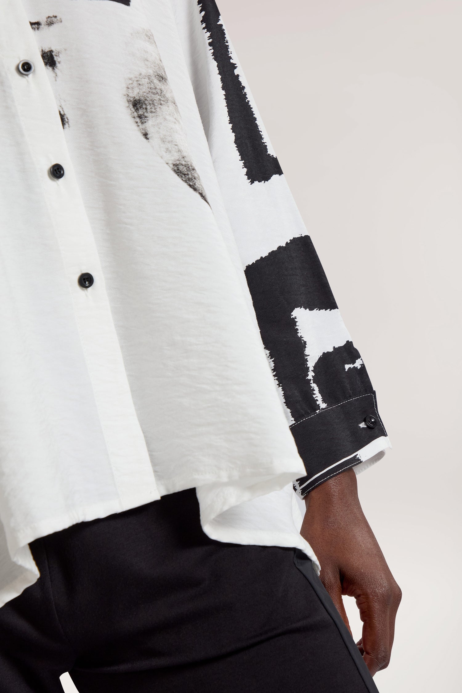 Close-up of a person wearing the Viscose Print Easy Shirt in white with black abstract patterns, paired with black pants. Only the torso and part of an arm are visible.