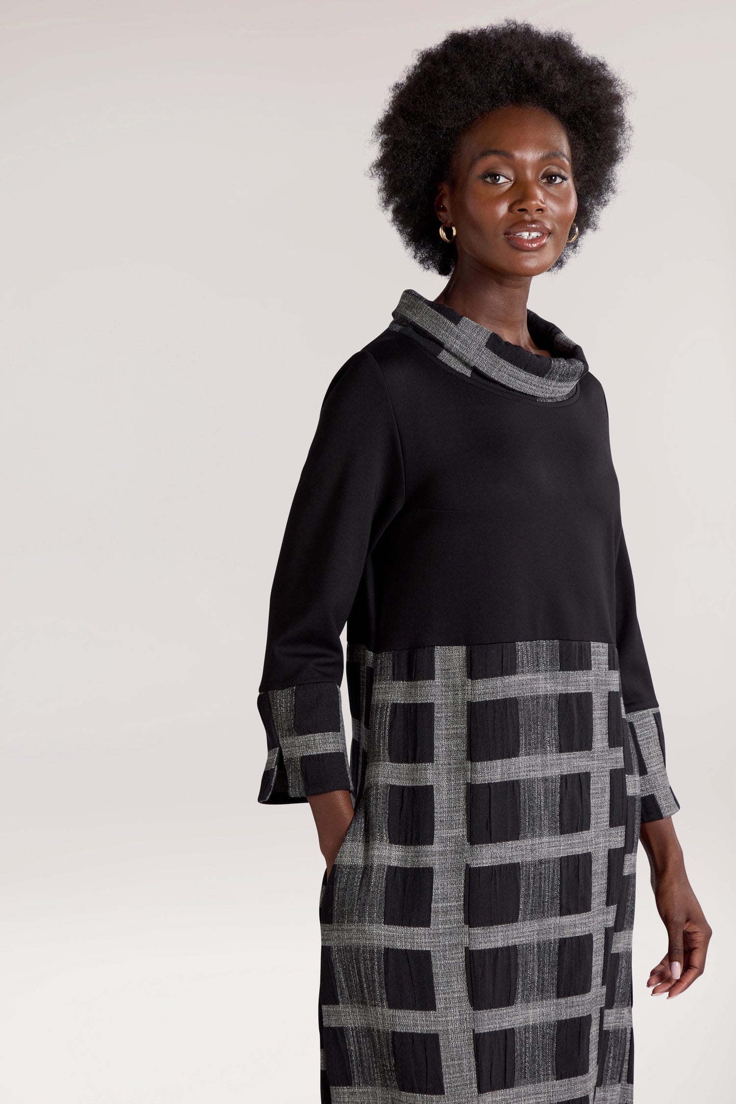 A woman with an afro hairstyle wearing a Checked Cowl Neck Dress stands and poses against a neutral background.