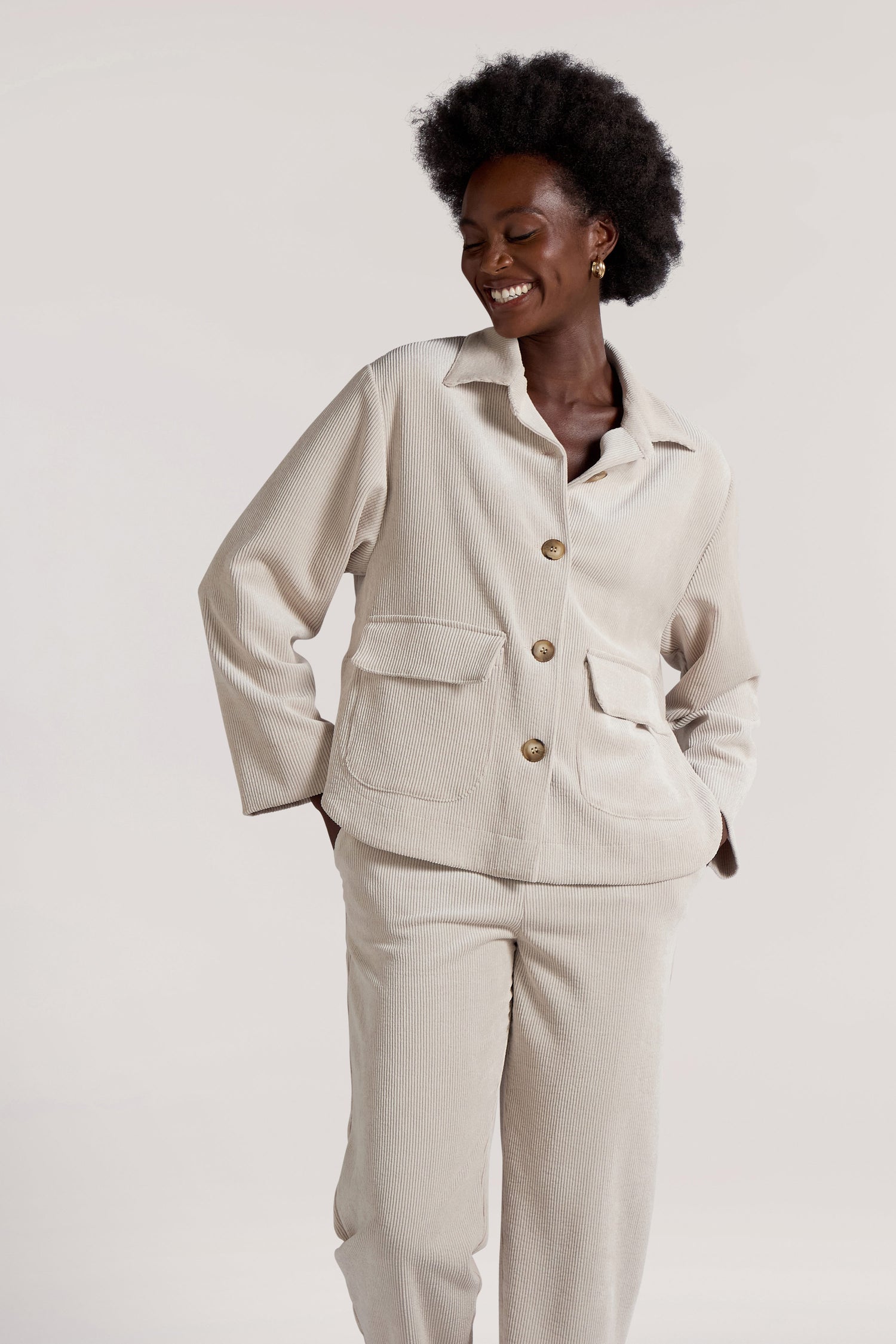 A person wearing the Cord Jacket in a cream color, along with matching minimalist pants, is smiling against a plain background.