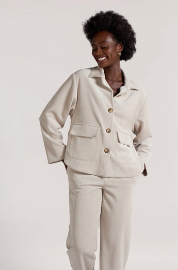 A person wearing the Cord Jacket in a cream color, along with matching minimalist pants, is smiling against a plain background.