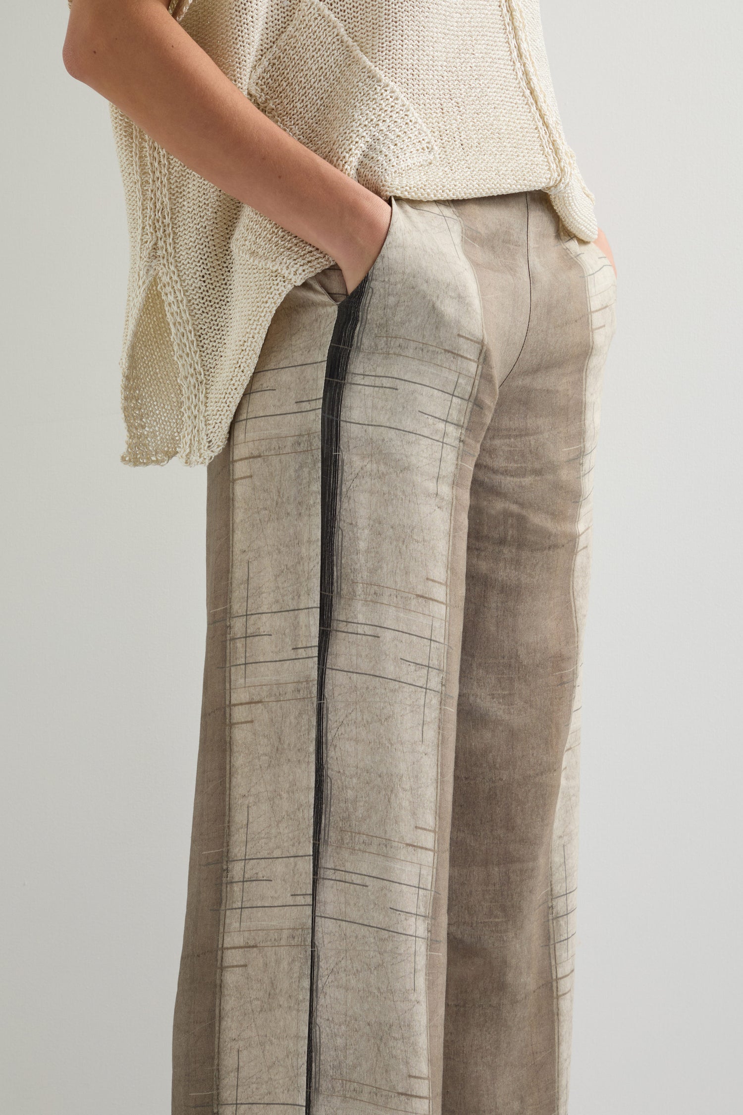 A person in a beige knit top and Wide Stripe Trouser crafted from lightweight, breathable fabric, showcasing a relaxed wide-leg silhouette with hands casually tucked into the pockets.