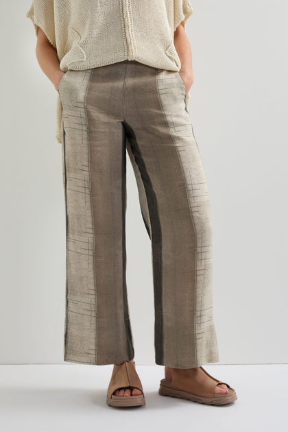 A person wears Wide Stripe Trousers, featuring a relaxed wide-leg silhouette with vertical stripes, crafted from lightweight breathable fabric. They're paired with brown sandals and the person's hands rest casually in their pockets against a plain background.