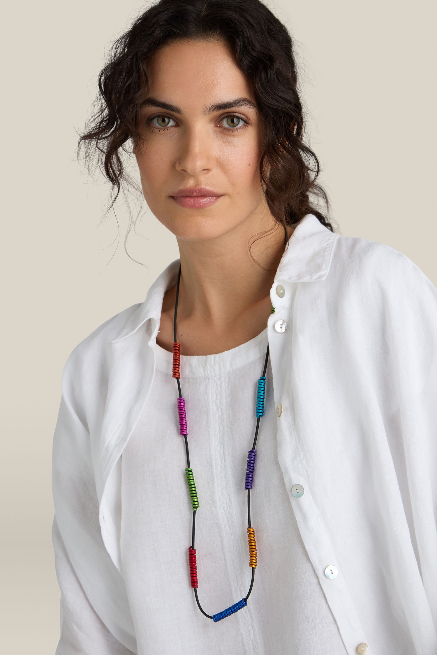 Woman wearing a white shirt and a long, colorful Rainbow Spirals Necklace by Oana Millet, posing against a plain background.