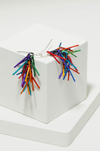 Fringe Earrings, a pair of unique, brightly colored aluminium earrings, displayed on a white geometrical pedestal.