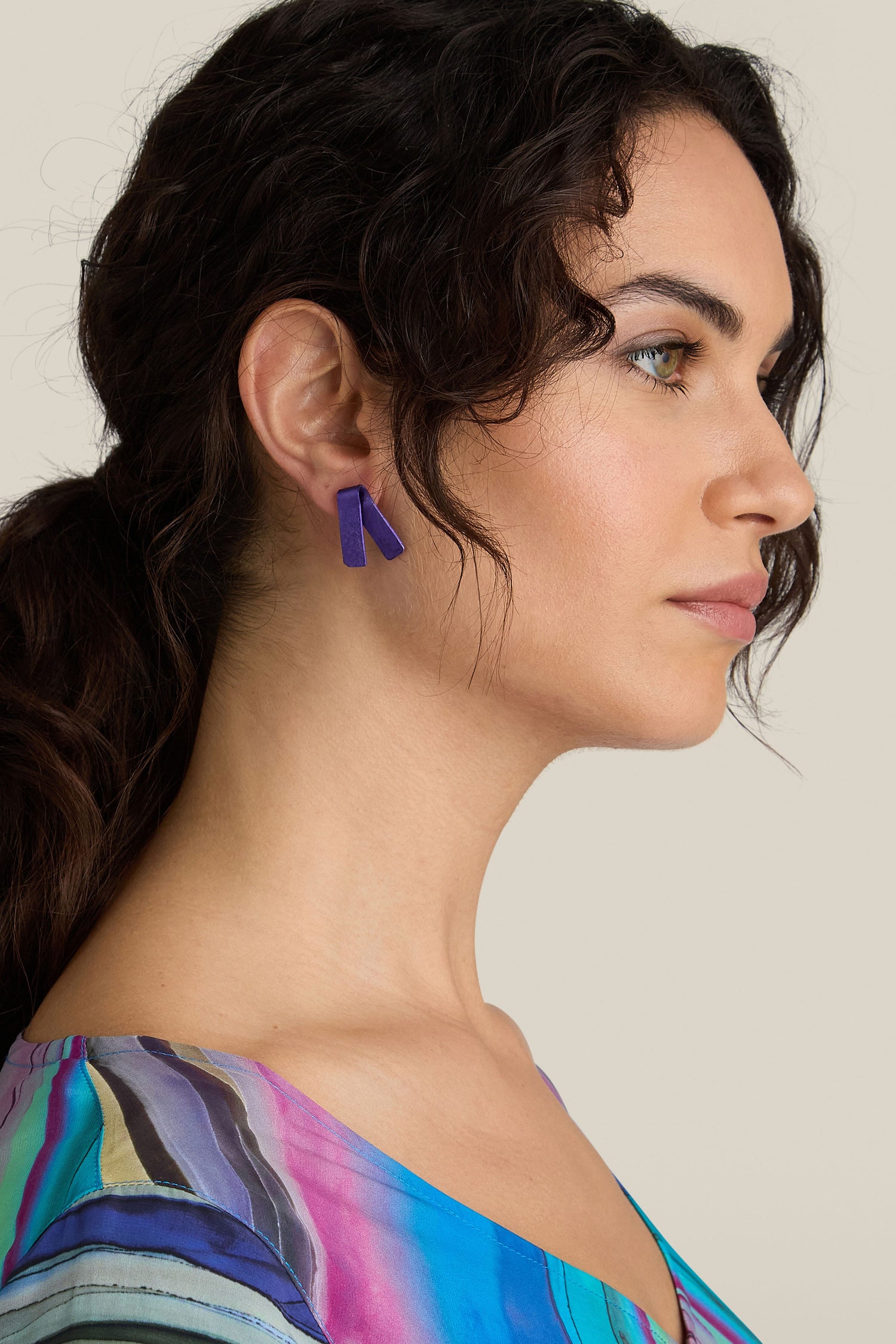 A person with long, dark hair tied back is wearing vibrant, handmade Origami Earrings crafted from aluminum and a colorful top, shown in profile view against a neutral background.