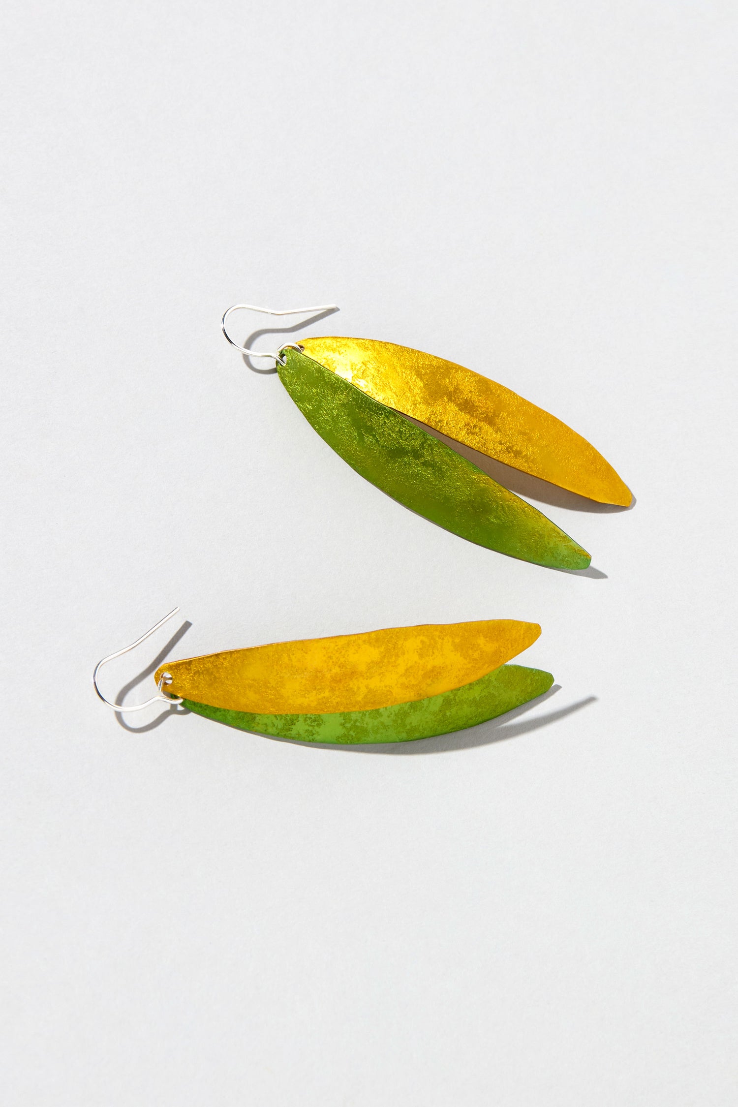 The Aluminium Leaves Earrings feature striking metallic gold and green leaf-like shapes on a white background. Perfect for bold fashion statements, they elegantly blend nature-inspired design with sophistication.