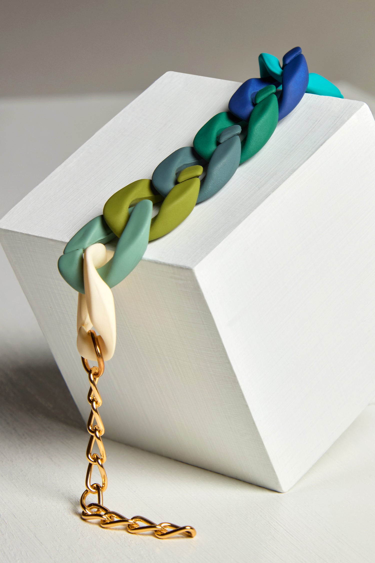 The Colour Pop Link Necklace, with its chunky multicolored links and gold clasp, drapes over a white geometric block, making a vibrant statement piece.