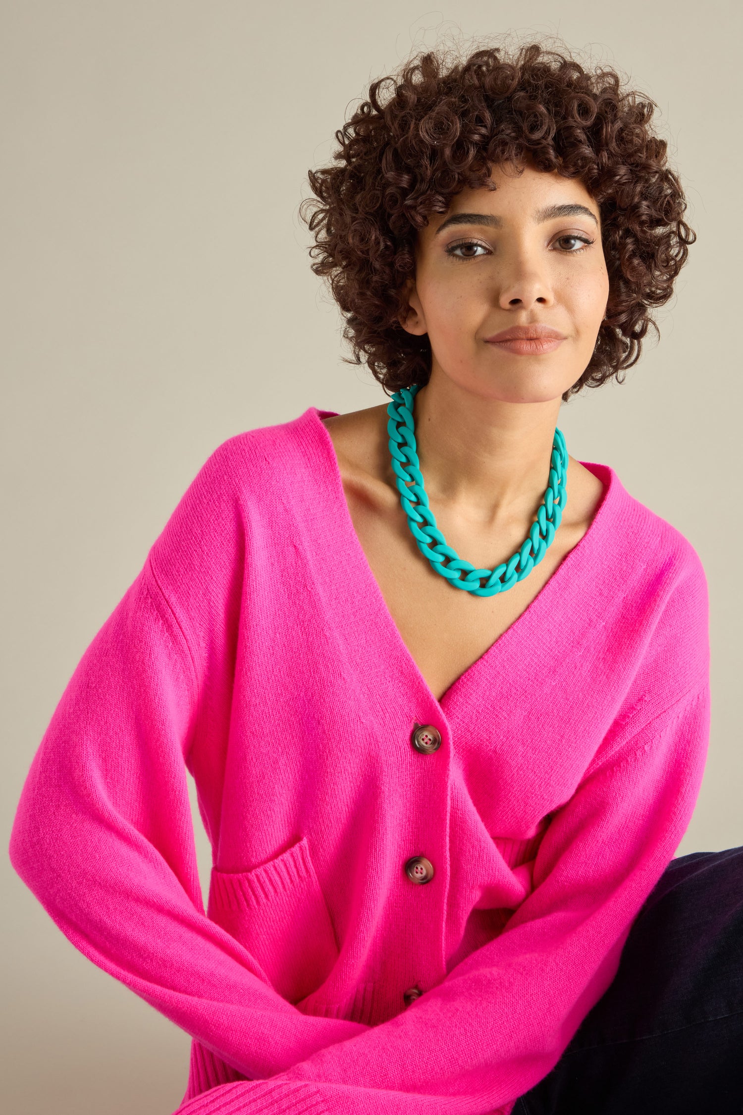 Person wearing a bright pink cardigan and a Colour Pop Link Necklace, adding bold accessories to their look, sits against a neutral background.