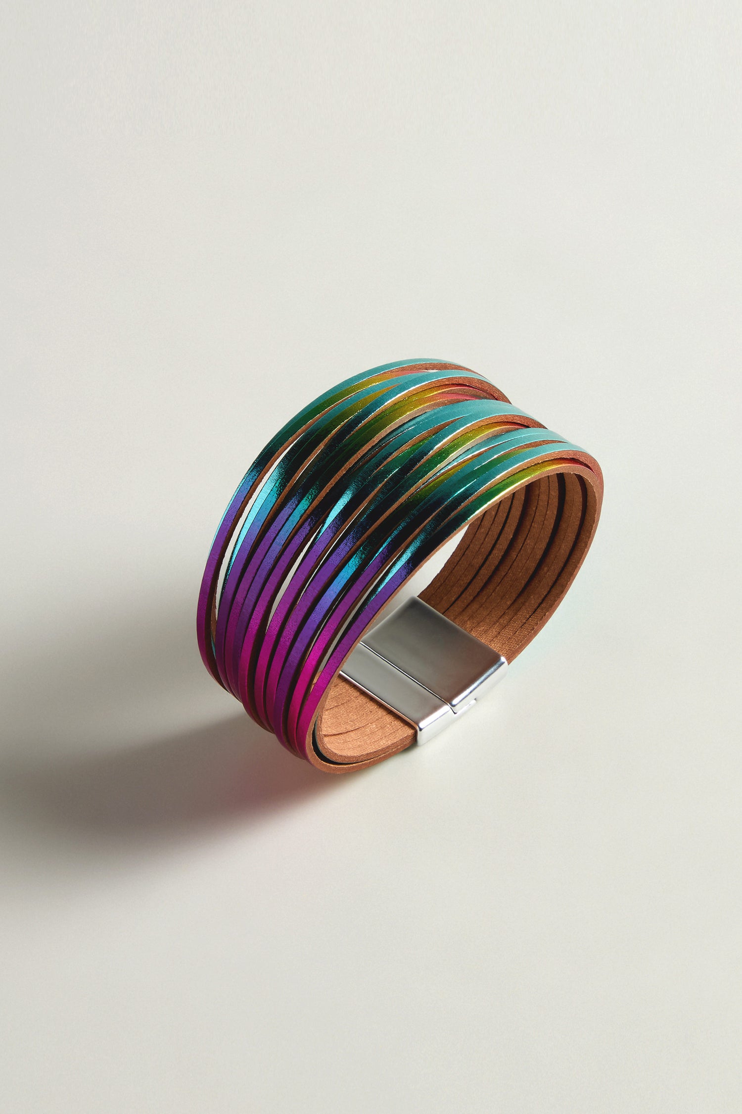 The Woven Metallic Bracelet showcases iridescent colors with leatherette threads and a metallic finish clasp, set against a plain backdrop.