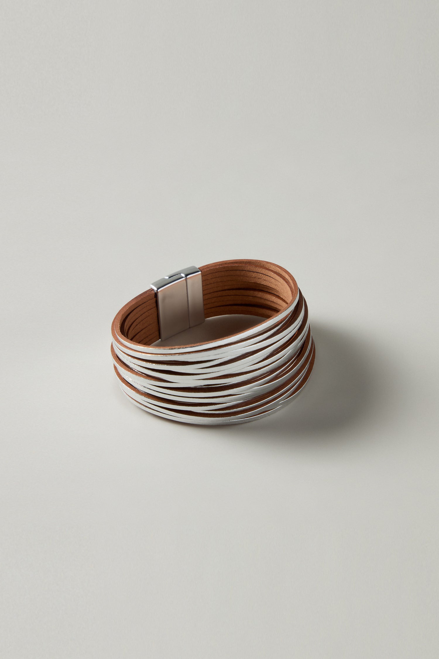 The Woven Metallic Bracelet features interwoven brown and white leatherette strands with a chic metallic clasp, depicted against a plain gray background.