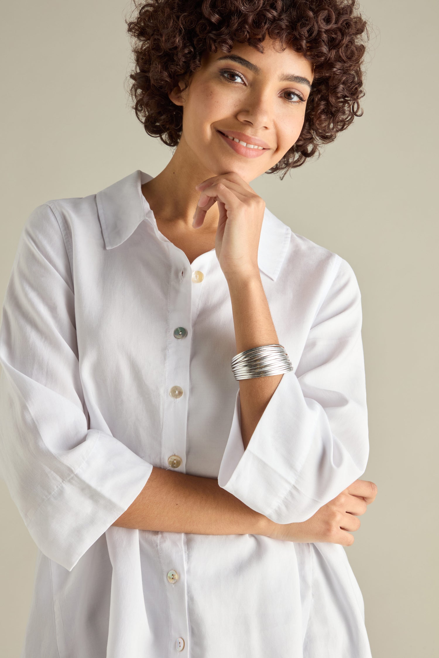 A person with curly hair smiles, wearing a white shirt and a large Woven Metallic Bracelet featuring a magnetic clasp, standing against a plain background.