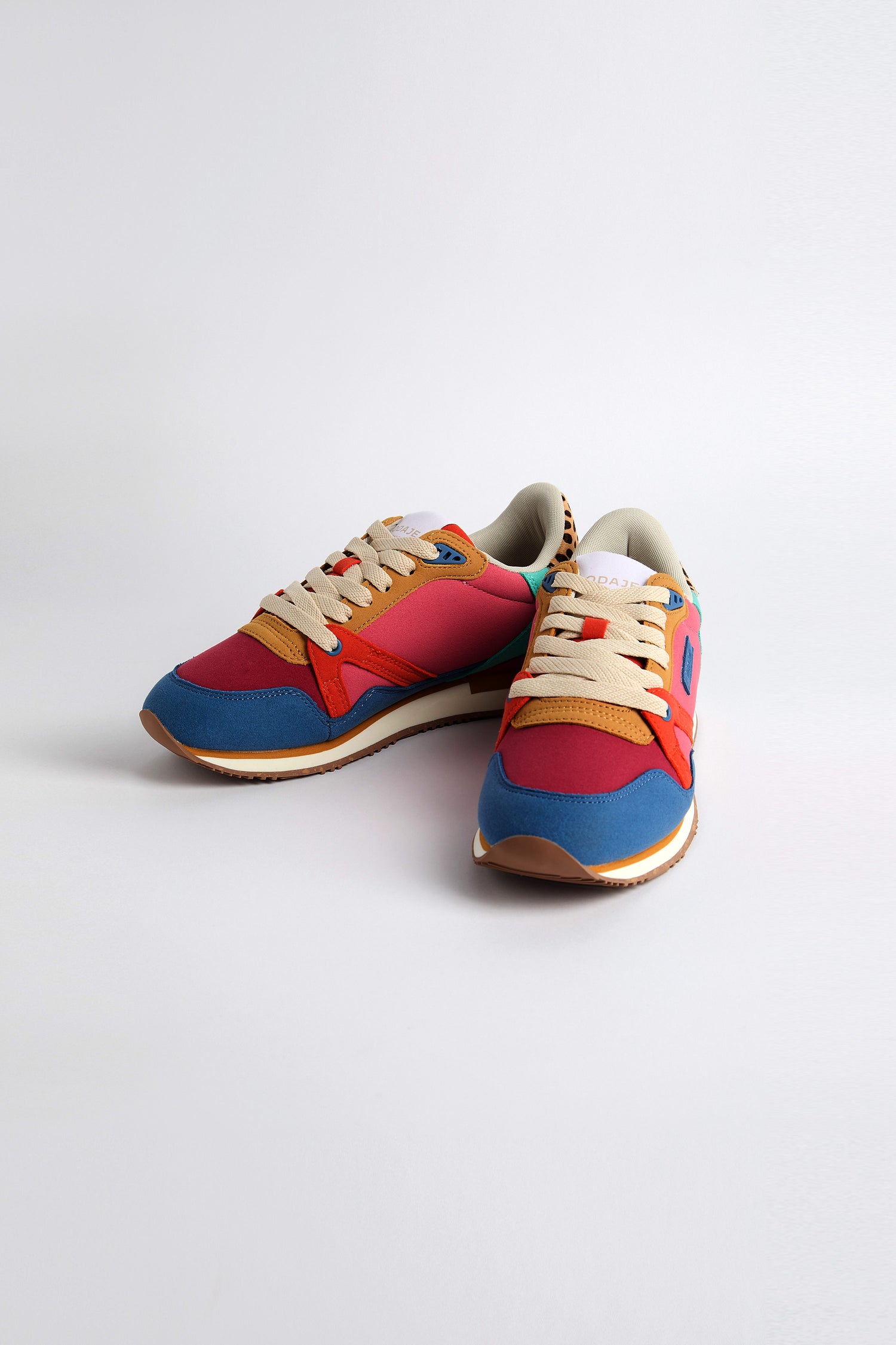 The Andree Trainers showcase a vibrant design with red, blue, and beige vegan suede panels, enhanced by beige laces and a white sole—all elegantly displayed on a plain white background.