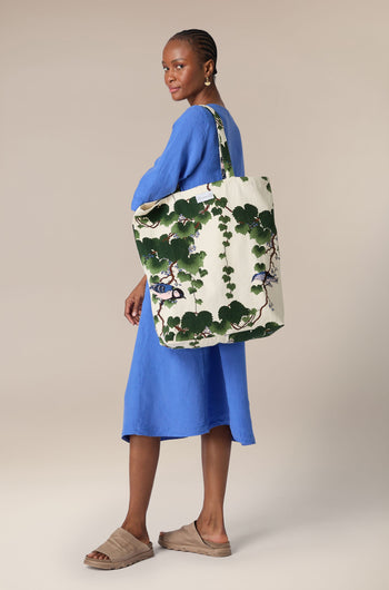 Woman in a blue dress holding a large floral-patterned, sustainable cotton Acer Canvas Bag.