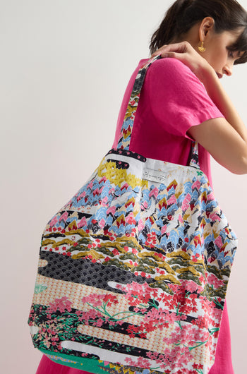 A person in a pink dress displays a large Spring Print Canvas Bag, featuring a vibrant pattern, against a light background.