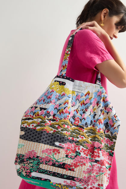 A person in a pink dress displays a large Spring Print Canvas Bag, featuring a vibrant pattern, against a light background.