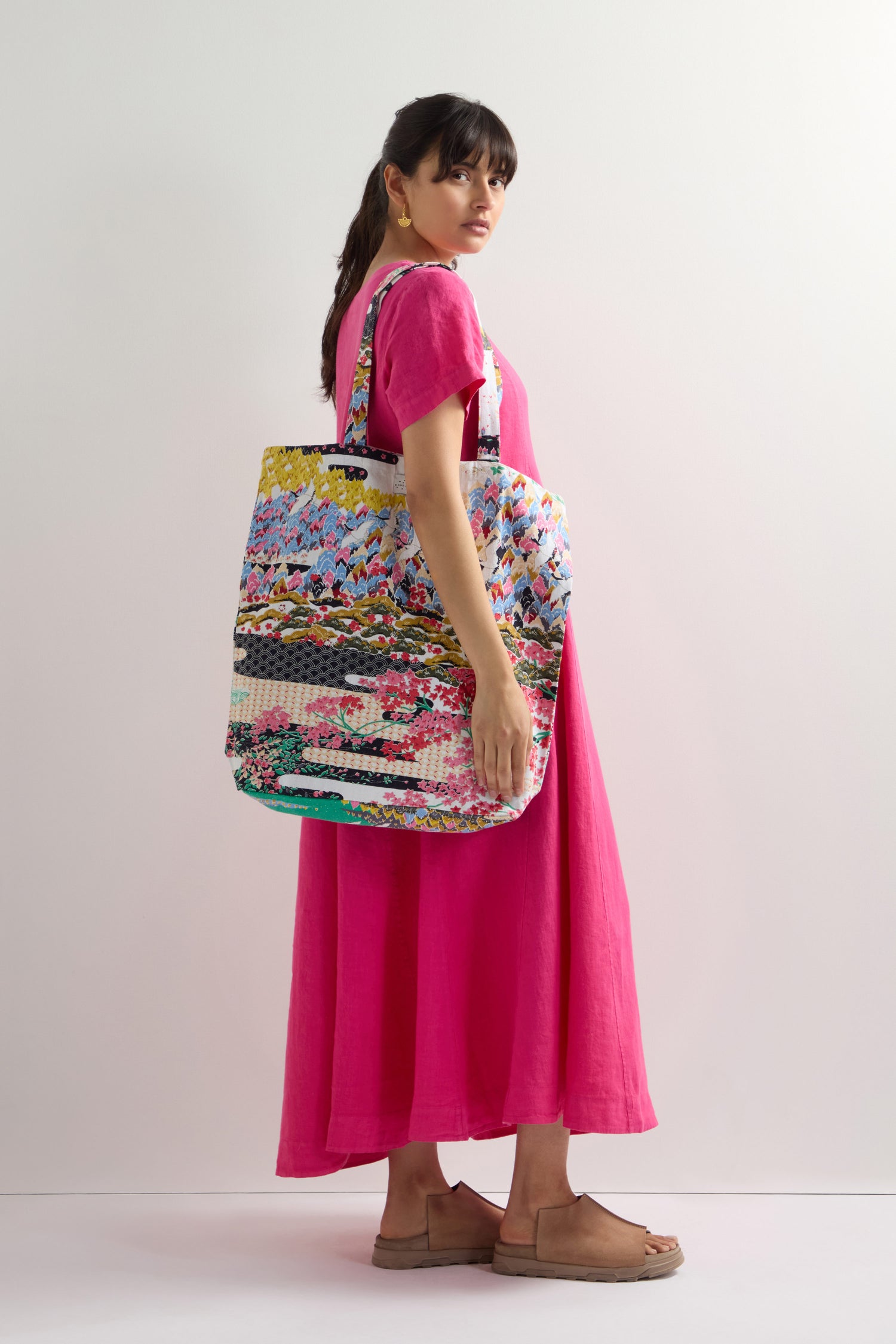 Against a plain white background, a person in a bright pink dress and brown sandals carries the vibrant "Spring Print Canvas Bag" crafted from sustainable cotton.